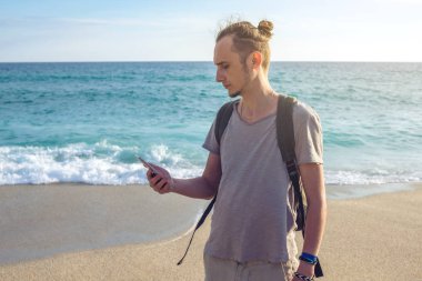 Adam Gezgin ile onun smartphone vasıl deniz ve okyanus dalgaları arka plan üzerinde seyir sırt çantası.