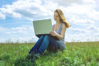 Yeşil çayır bulutlu gökyüzü arka plan üzerinde oturan ve çalışma veya kablosuz laptop ile eğitim kadın