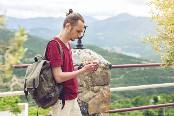 Hombre viajero con mochila mirando su teléfono inteligente en el fondo de la naturaleza y las montañas — Foto de Stock