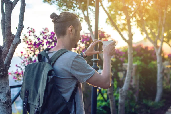Homem viajante com mochila faz uma foto em seu smartphone ao ar livre com montanhas no fundo — Fotografia de Stock