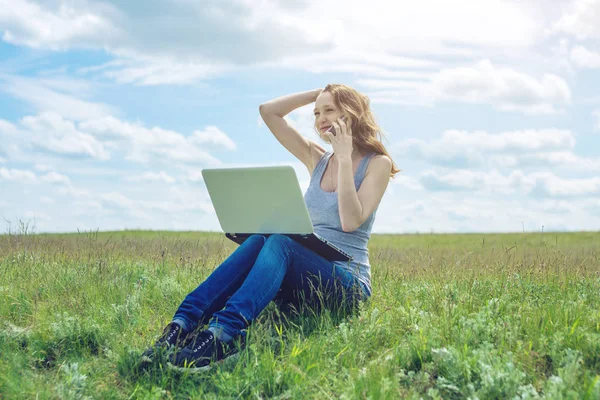 Femme assise sur une prairie verte sur le fond du ciel avec des nuages et travailler ou étudier avec un ordinateur portable sans fil — Photo