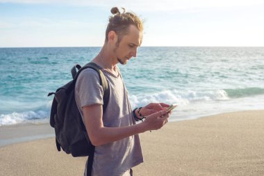 Adam Gezgin ile onun smartphone vasıl deniz ve okyanus dalgaları arka plan üzerinde seyir sırt çantası.