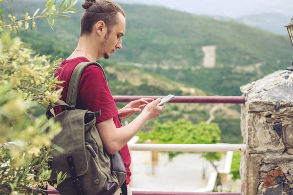 Hombre viajero con mochila mirando su teléfono inteligente en el fondo de la naturaleza y las montañas — Foto de Stock