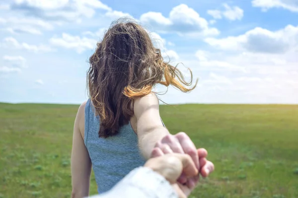 Siga-me, menina morena atraente segurando a mão das pistas em um campo verde limpo, estepe com nuvens — Fotografia de Stock