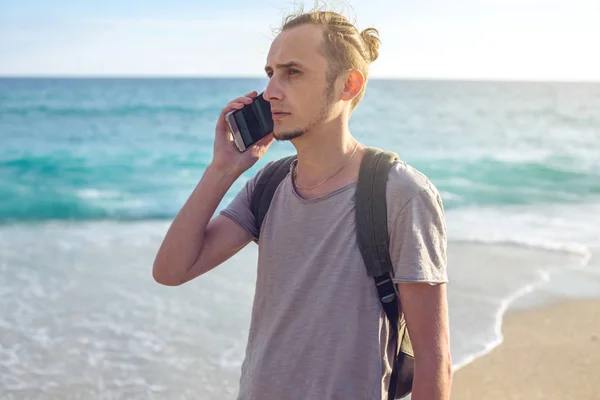 Человек путешественник с рюкзаком разговаривает по телефону на заднем плане море и волны океана — стоковое фото