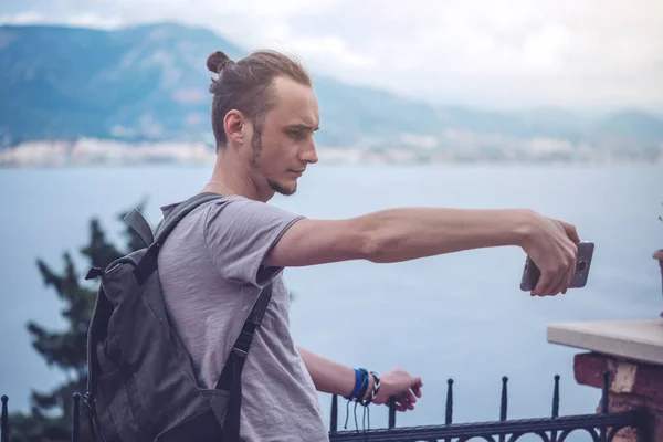 Человек путешественник с рюкзаком делает фото на вашем смартфоне на открытом воздухе с горами на заднем плане — стоковое фото