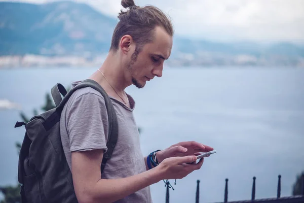 Человек путешественник с рюкзаком глядя на свой смартфон на фоне природы и гор — стоковое фото