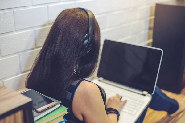 Chica con auriculares escuchando lecciones o audiolibros en el teléfono y trabajando en el ordenador portátil. Concepto de educación tecnológica —  Fotos de Stock
