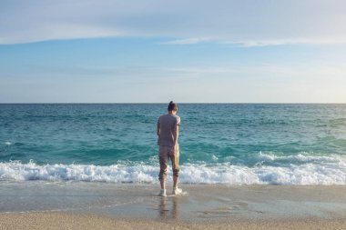 Deniz ve kıyı kumda ayak izleri bırakmak için ıslak spor ayakkabı içinde yürüyen genç mutlu adam