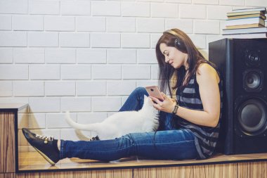 Kadın bir audiobook ile kedi duvar arka plan üzerinde oturan bir telefon dinleme kulaklık