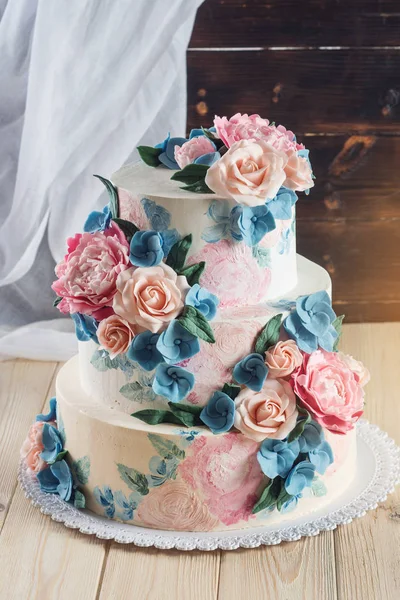 Um belo casamento caseiro bolo de três camadas decorado com rosas rosa e flores azuis em um estilo rústico na mesa de madeira — Fotografia de Stock