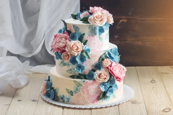 Una bella casa di nozze torta a tre livelli decorata con rose rosa e fiori blu in stile rustico su tavolo di legno — Foto Stock