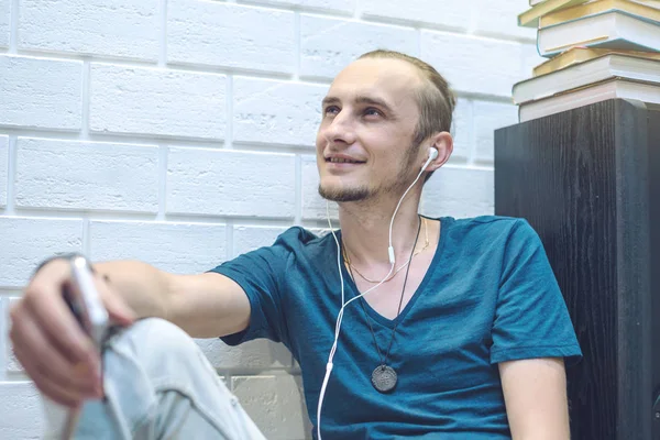 Hombre joven en auriculares escuchando el libro de audio en el entorno del hogar. Concepto de tecnología y educación moderna — Foto de Stock