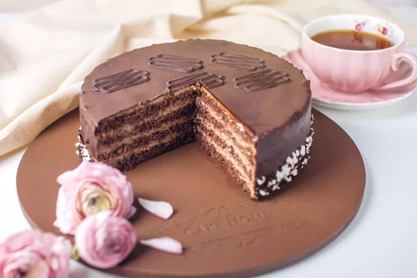 Вкусный шоколадный торт с нугой и бисквитом в порезах. Подаваемые цветы розы и розовая чашка чая — стоковое фото