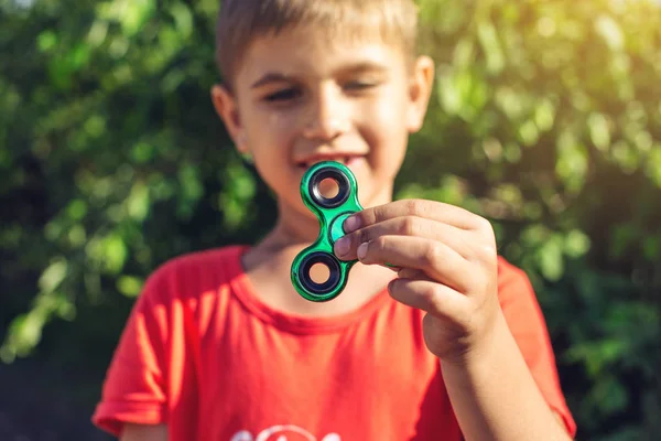 Un chico juega con el spinner girándolo en su mano al aire libre. Tendencias en los juguetes antiestrés para niños — Foto de Stock