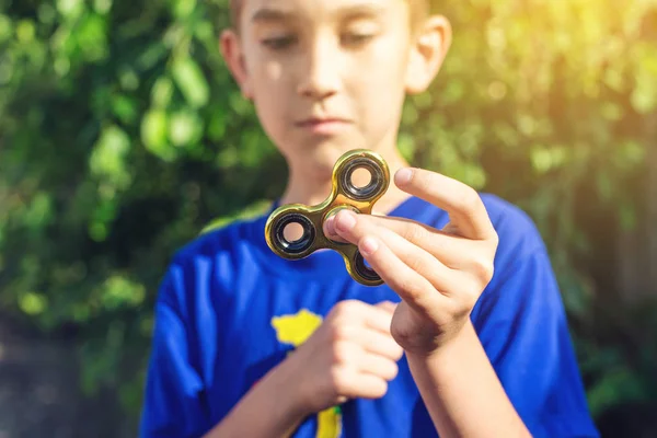 Un garçon joue avec spinner le tordant dans sa main à l'extérieur. Tendances dans les jouets anti-stress pour enfants — Photo