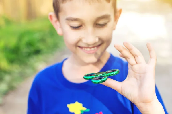Un chico juega con el spinner girándolo en su mano al aire libre. Tendencias en los juguetes antiestrés para niños — Foto de Stock