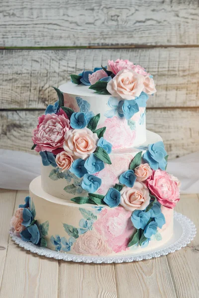 Eine schöne dreistöckige Hochzeitstorte mit rosa Rosen und blauen Blumen im rustikalen Stil auf einem Holztisch — Stockfoto