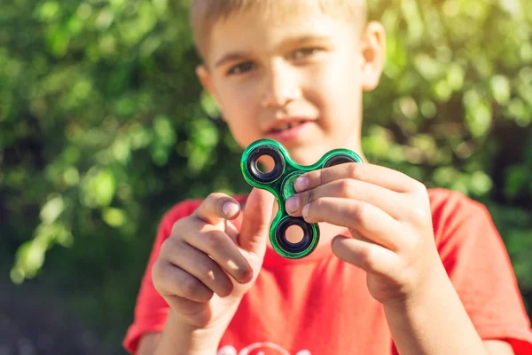 Un garçon joue avec spinner le tordant dans sa main à l'extérieur. Tendances dans les jouets anti-stress pour enfants — Photo