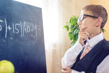 Okula dönüş. Akıllı çocuk sınıfta bir görev çözer. Çocuk tahtaya yazıyor. Kavram İlköğretim Okulu