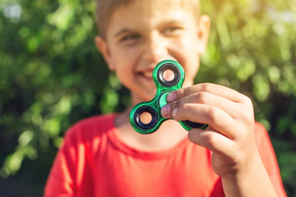 Un garçon joue avec spinner le tordant dans sa main à l'extérieur. Tendances dans les jouets anti-stress pour enfants — Photo