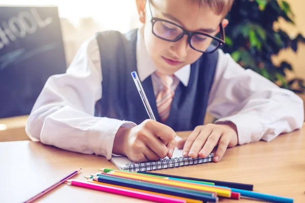 Vissza az iskolába. Aranyos gyerek ül a tanteremben a íróasztal. Fiú a tanulás tanulságok írja egy tollat a notebook — Stock Fotó