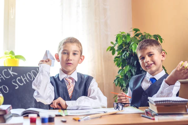 Vissza az iskolába. Aranyos gyerek ül a tanteremben a íróasztal. Fiúk színészet dobott egy papír sík. — Stock Fotó