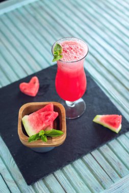 Karpuz ve nane bir mavi ahşap zemin üzerine dilimlenmiş parçaları ile bir bardak taze kırmızı yüzlü. Yaz soğuk içecekler
