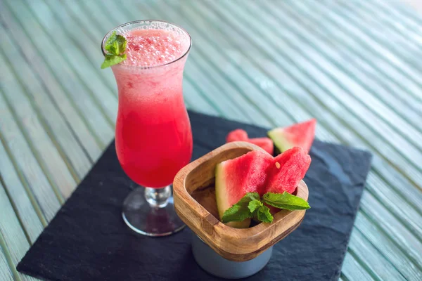 Karpuz ve nane bir mavi ahşap zemin üzerine dilimlenmiş parçaları ile bir bardak taze kırmızı yüzlü. Yaz soğuk içecekler