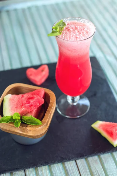 Batido rojo fresco en un vaso con trozos de sandía en rodajas y menta sobre un fondo de madera azul. Bebidas frescas de verano — Foto de Stock