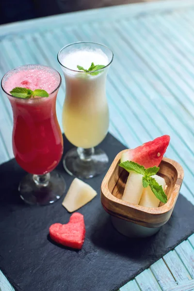 Batido fresco en un vaso con trozos de sandía en rodajas y melón con menta sobre fondo azul. Bebidas frescas de verano — Foto de Stock