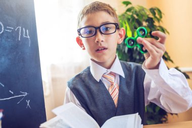 Okula dönüş. Şirin çocuk sınıfta masasında oturuyor. Ders sırasında bir spinner ile oynayan çocuk