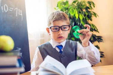 Okula dönüş. Şirin çocuk sınıfta masasında oturuyor. Ders sırasında bir spinner ile oynayan çocuk