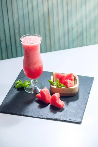 Batido rojo fresco en un vaso con trozos de sandía en rodajas y menta sobre un fondo de madera azul. Bebidas frescas de verano — Foto de Stock