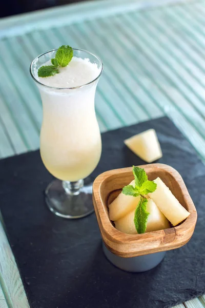 Čerstvý bílý smoothie ve sklenici s nakrájené kousky melounu a máty na modrém pozadí dřevěná. Letní studené nápoje — Stock fotografie