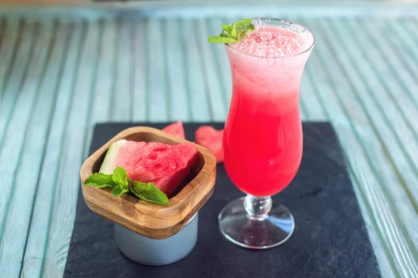 Batido rojo fresco en un vaso con trozos de sandía en rodajas y menta sobre un fondo de madera azul. Bebidas frescas de verano — Foto de Stock