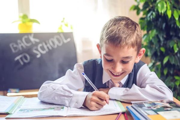 Vissza az iskolába. Aranyos gyerek ül a tanteremben a íróasztal. Fiú a tanulás tanulságok írja egy tollat a notebook — Stock Fotó