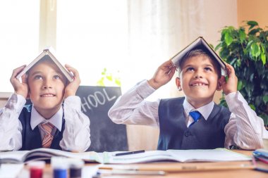 Okula dönüş. Şirin çocuk sınıfta masasında oturuyor. Çocuklar çok yaramazsın ve kafa üzerinde kitap tutun