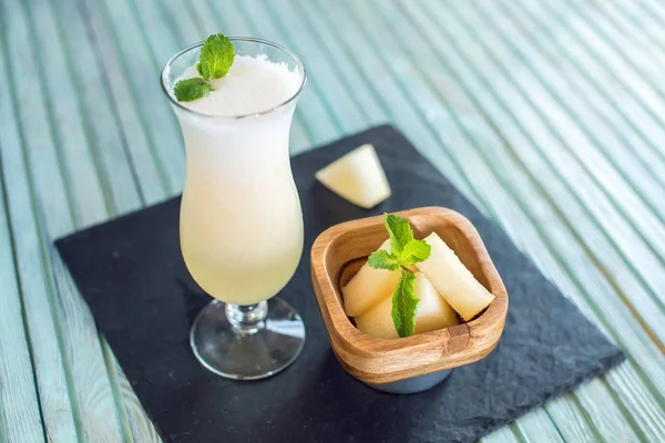 Čerstvý bílý smoothie ve sklenici s nakrájené kousky melounu a máty na modrém pozadí dřevěná. Letní studené nápoje — Stock fotografie