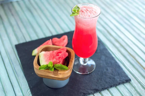 Batido rojo fresco en un vaso con trozos de sandía en rodajas y menta sobre un fondo de madera azul. Bebidas frescas de verano — Foto de Stock