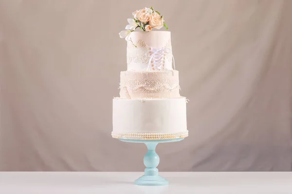 Un gran pastel de boda por niveles en forma de vestido con encaje decorado con rosas rosadas en la parte superior de la mesa . —  Fotos de Stock