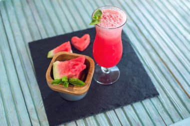 Karpuz ve nane bir mavi ahşap zemin üzerine dilimlenmiş parçaları ile bir bardak taze kırmızı yüzlü. Yaz soğuk içecekler