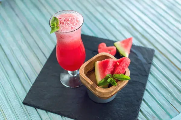 Batido rojo fresco en un vaso con trozos de sandía en rodajas y menta sobre un fondo de madera azul. Bebidas frescas de verano — Foto de Stock