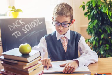 Okula dönüş. Şirin çocuk sınıfta masasında oturuyor. Üzerine ders kitap okurken erkek