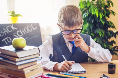 Okula dönüş. Şirin çocuk sınıfta masasında oturuyor. Çocuk ders içinde a defter bir kalem yazar öğrenme