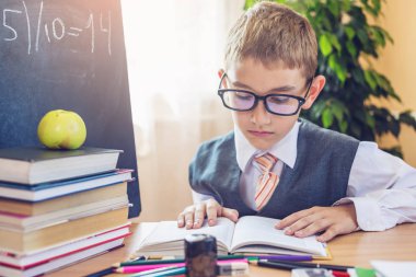 Okula dönüş. Şirin çocuk sınıfta masasında oturuyor. Üzerine ders kitap okurken erkek