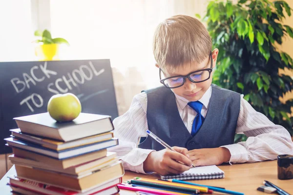 Vissza az iskolába. Aranyos gyerek ül a tanteremben a íróasztal. Fiú a tanulás tanulságok írja egy tollat a notebook — Stock Fotó