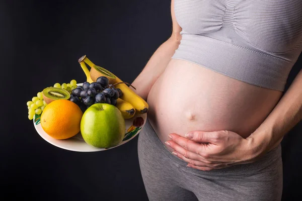 Uma mulher grávida com barriga segurando um prato com frutas. Conceito para controle de peso e alimentação saudável durante a gravidez — Fotografia de Stock