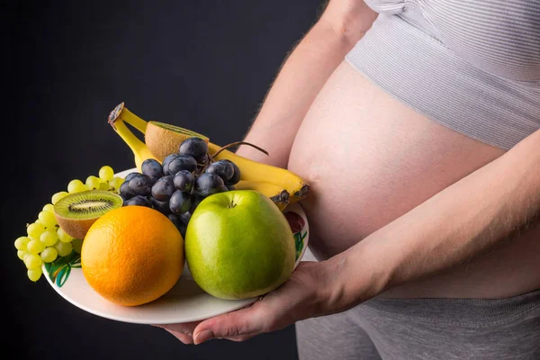 Uma mulher grávida com barriga segurando um prato com frutas. Conceito para controle de peso e alimentação saudável durante a gravidez — Fotografia de Stock