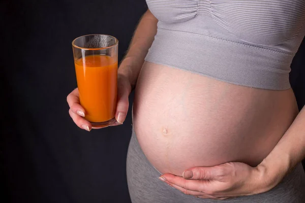 Terhes nő hasa egy pohár sárgarépalé a kezében tartja. Koncepció súlykontroll és az egészséges táplálkozás — Stock Fotó